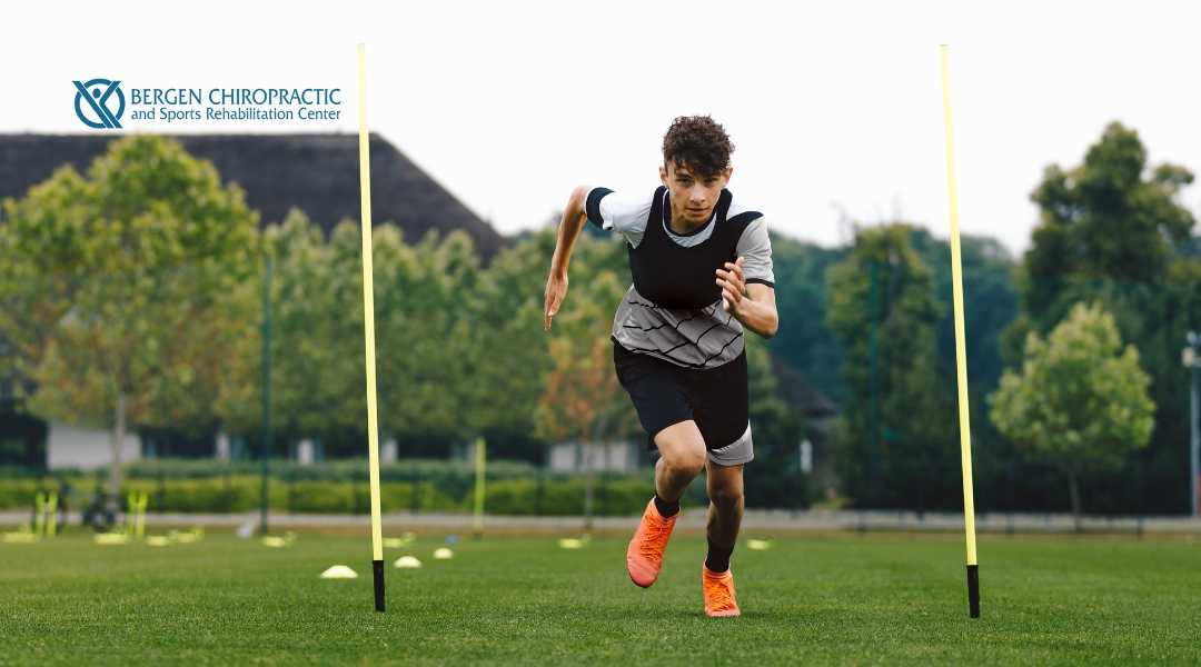 A young athlete is sprinting forward on a green field marked with yellow agility poles and cones