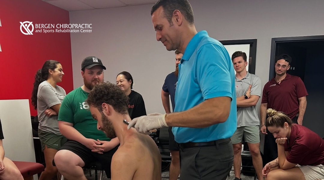 A hands-on chiropractic seminar in session as a clinician demonstrates upper back treatment using soft tissue tools while participants observe and engage.
