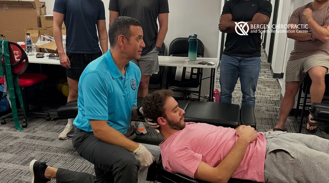 A chiropractor performs a neck mobilization technique on a lying participant while fellow attendees observe closely during an advanced clinical workshop at Bergen Chiropractic.