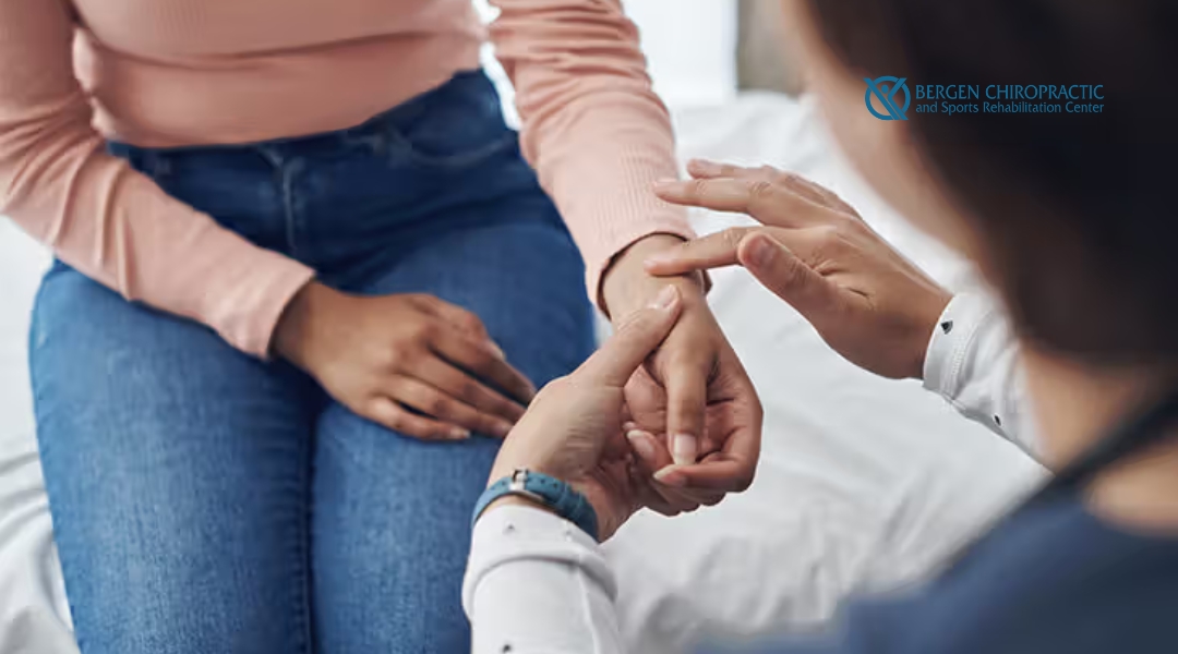 A chiropractor examines a female patient's wrist during a consultation, assessing joint mobility or nerve function, with the Bergen Chiropractic and Sports Rehabilitation Center logo displayed.