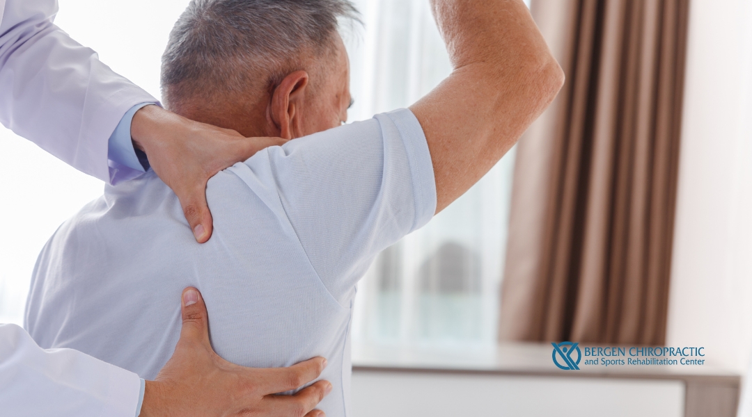 A chiropractor supports a senior man's shoulder during a mobility or posture assessment, emphasizing upper body care at Bergen Chiropractic and Sports Rehabilitation Center.