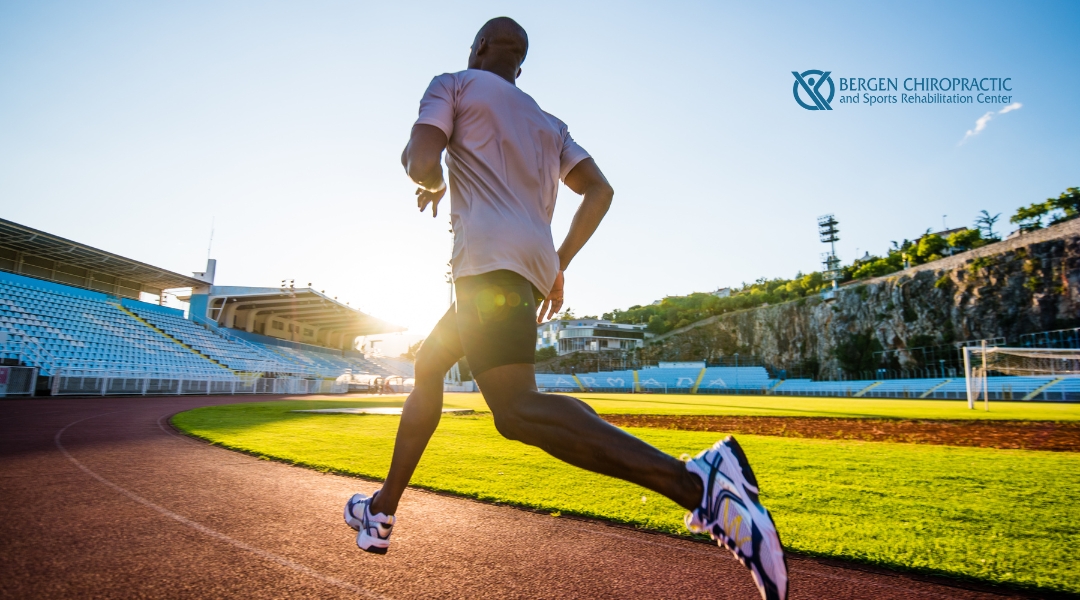 Male runner sprinting on a track at sunset, symbolizing restored movement and recovery after chiropractic care for IT band pain.