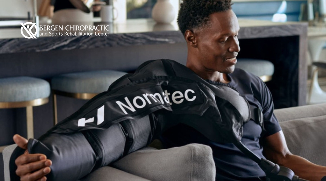 A man sits comfortably on a couch while receiving Normatec arm compression therapy at Bergen Chiropractic and Sports Rehabilitation Center.