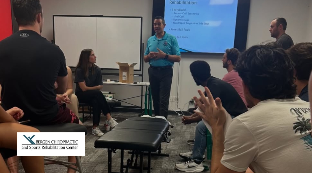 A chiropractor is leading a group session on rehabilitation techniques, with several individuals observing attentively.