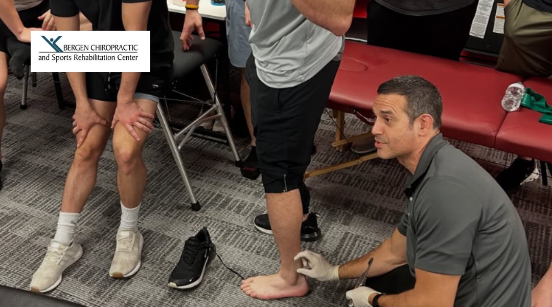 A chiropractor is assisting a patient in balancing on one leg during a session on lower extremity rehabilitation, with a group observing.