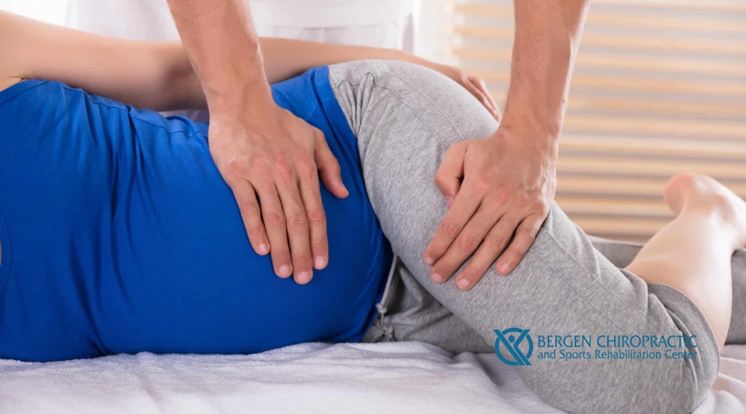 A chiropractor performing a spinal adjustment on a pregnant woman, with his hands on her back while she is lying on a treatment table.