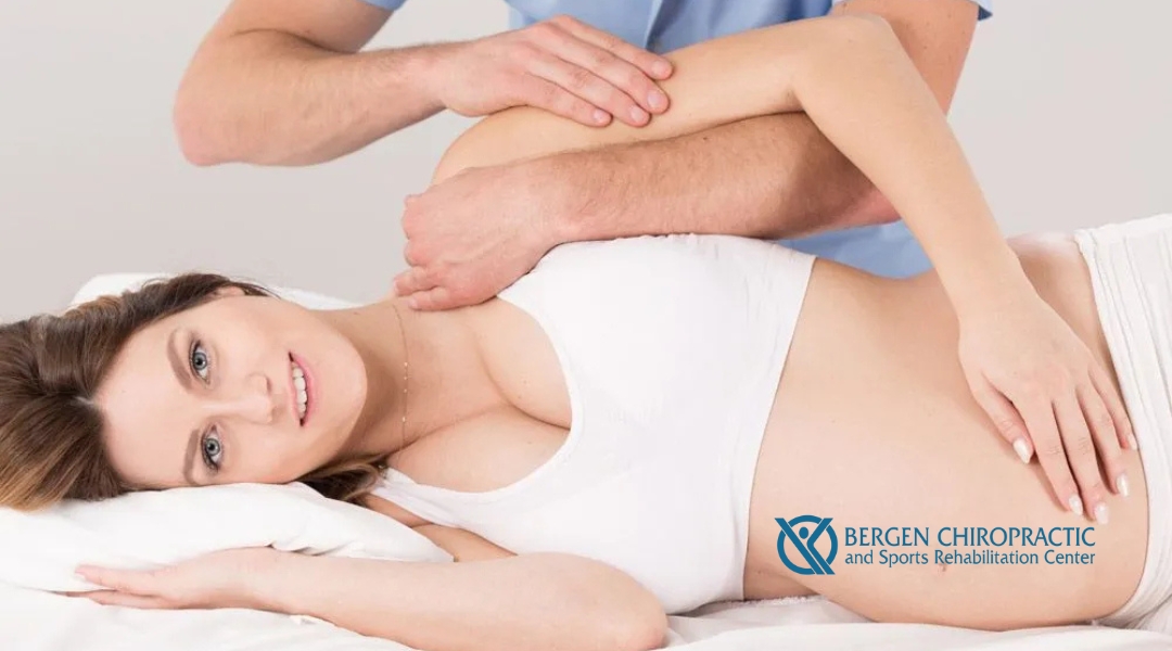 Pregnant woman receiving a chiropractic adjustment while lying on her side, supported by a chiropractor’s hands, at Bergen Chiropractic and Sports Rehabilitation Center.